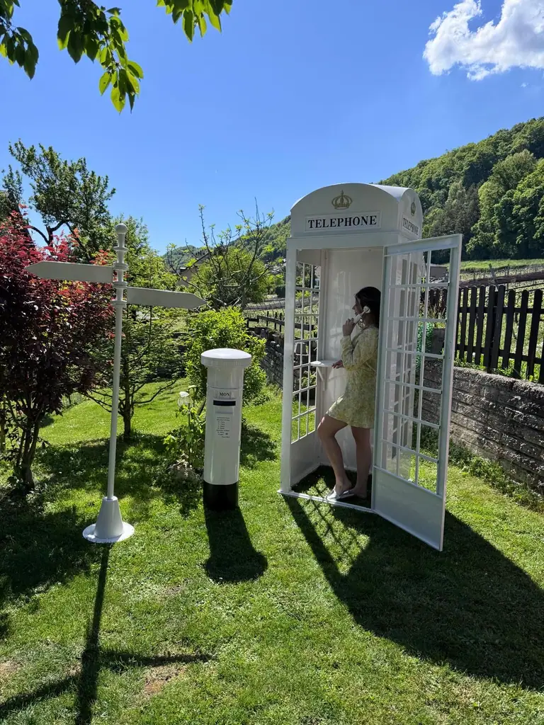 La cabine téléphonique londonienne blanche de COSAM dans un jardin, avec sa boîte aux lettres et son panneau directionnel