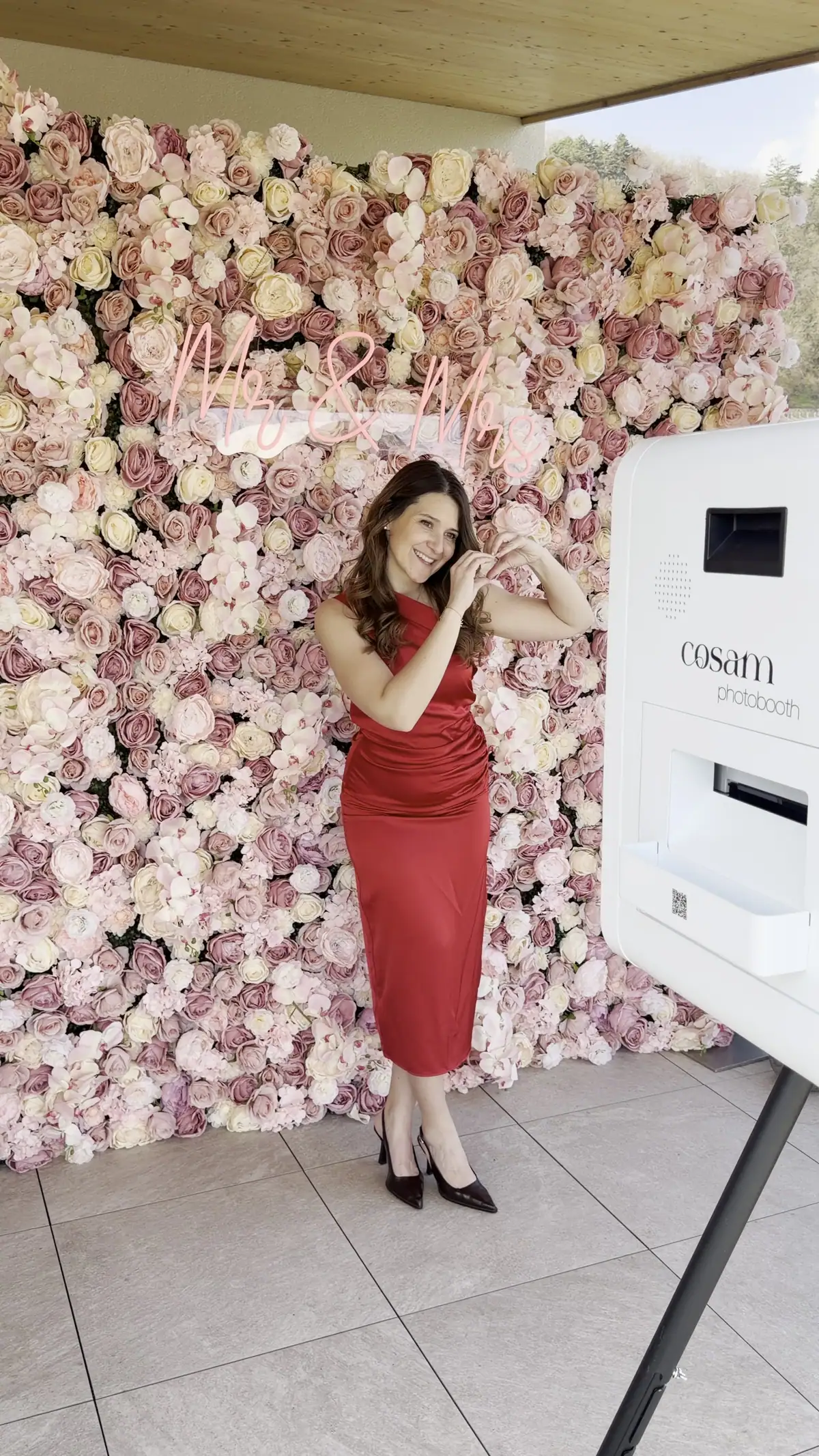 Une invitée pose devant le mur de roses COSAM, à côté du photobooth blanc