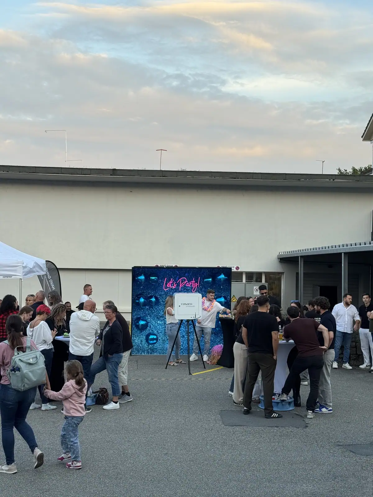 Les équipes Havo Group réunies en plein air devant le mur pailleté bleu et le photobooth, fête du personnel