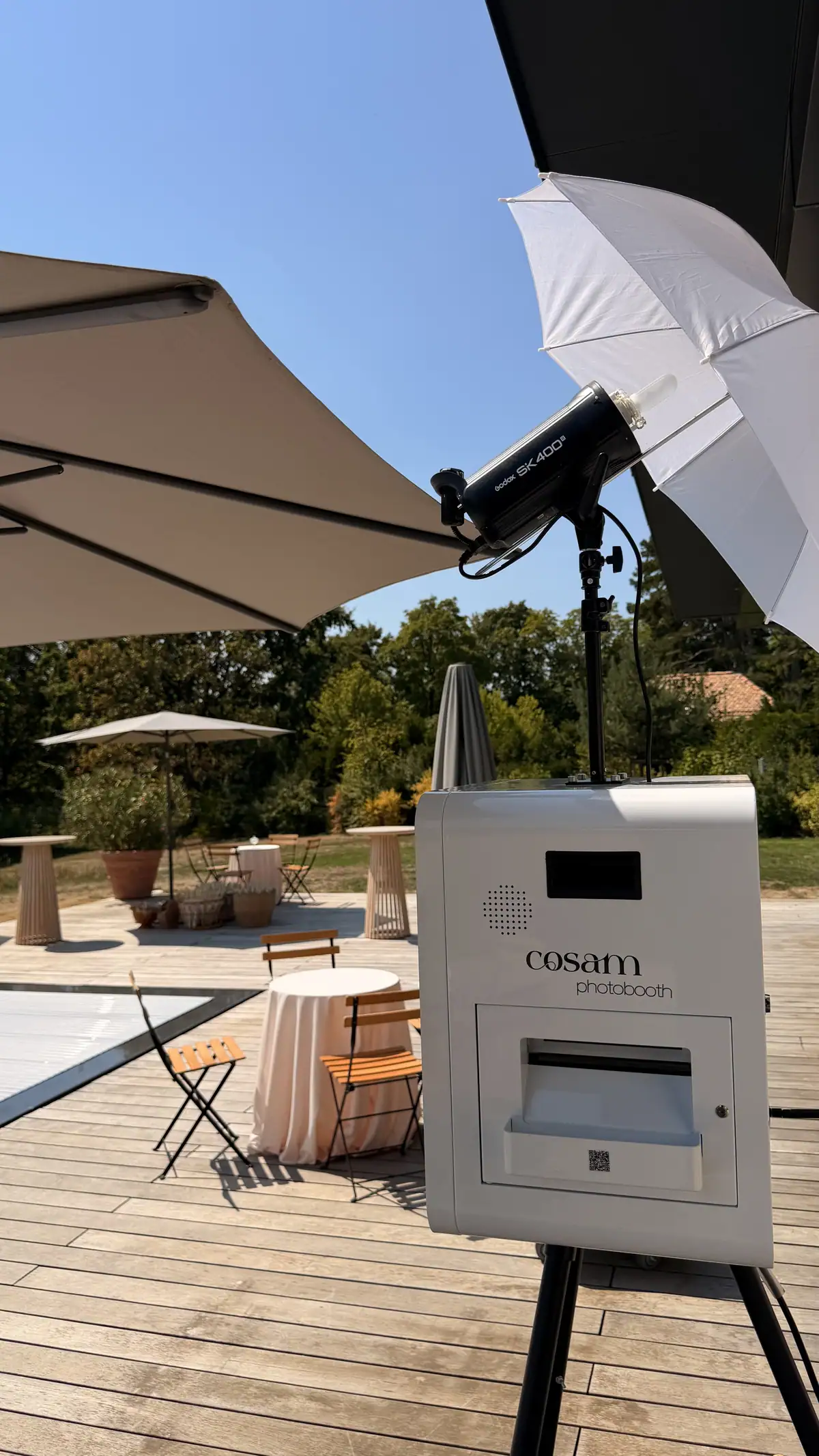 Le photobooth blanc COSAM installé en extérieur sur une terrasse en bois, au bord d'une piscine