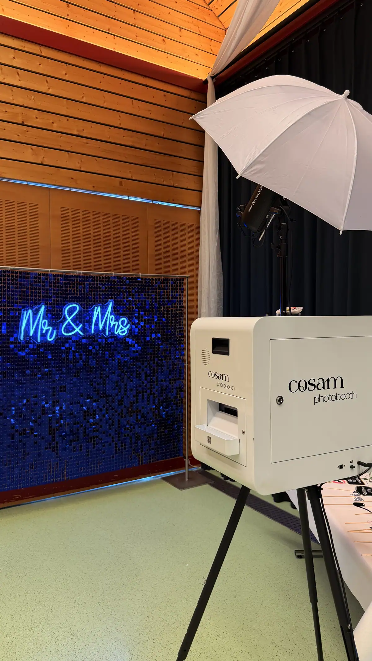 Le photobooth blanc COSAM devant le fond pailleté bleu et le néon « Mr & Mrs », lors d'un mariage