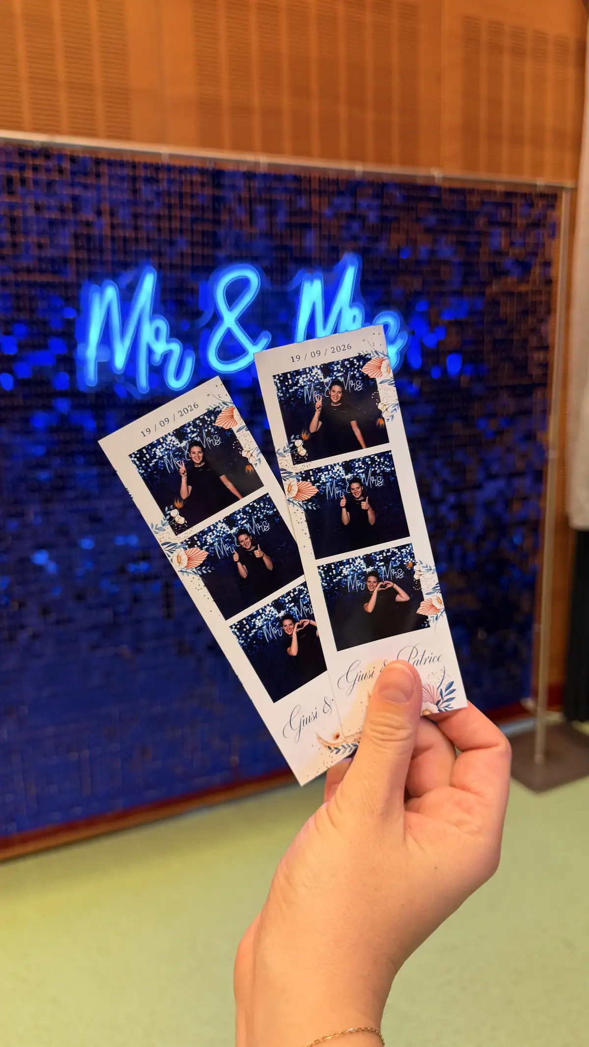 Deux bandelettes photo tenues devant le fond pailleté bleu et le néon « Mr & Mrs »
